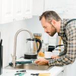 side-view-of-handsome-plumber-repairing-tap-with-m-MF6HLL7.jpg